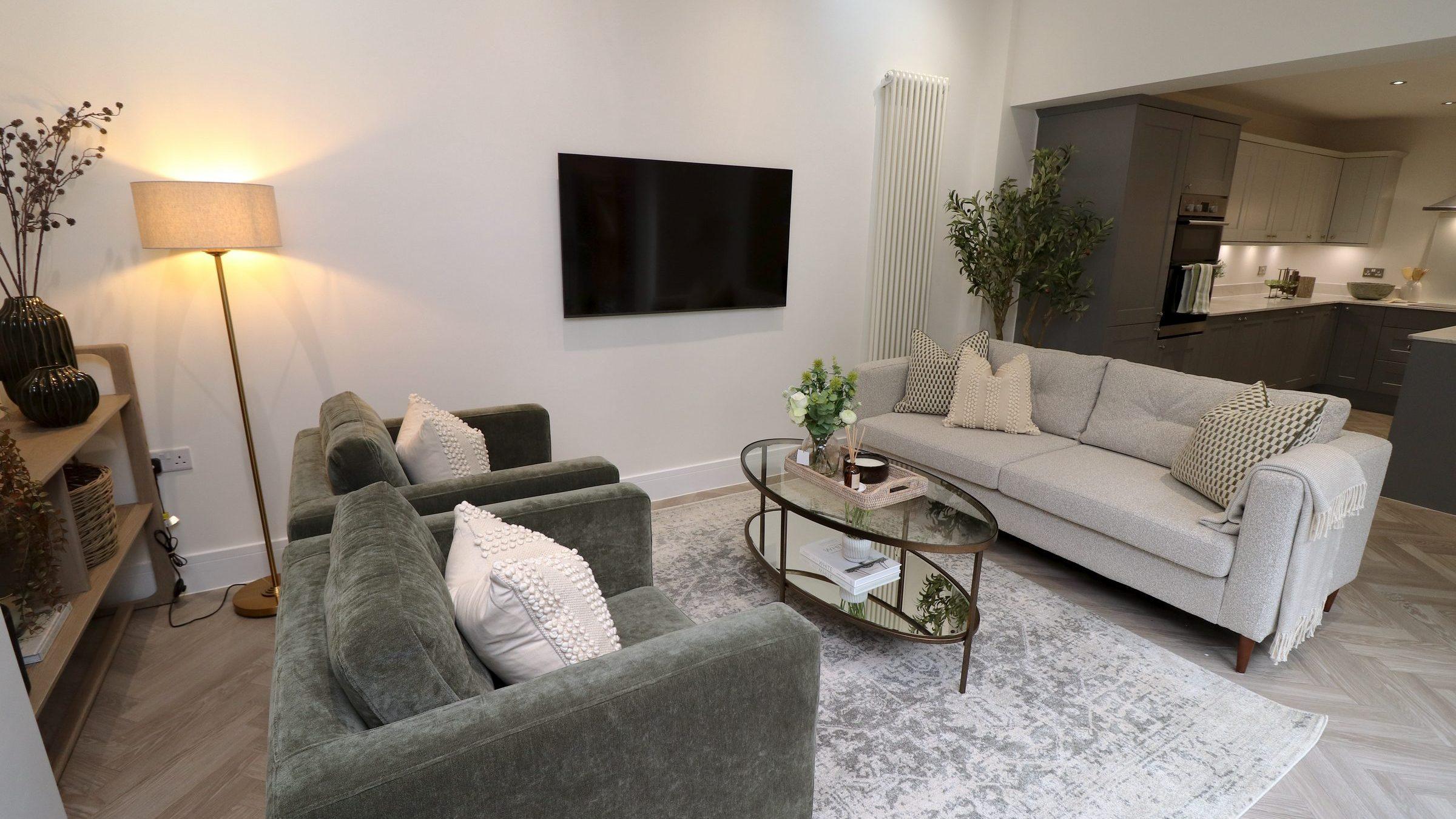Staged family room: grey sofa, olive armchairs, a floor lamp and an olive tree beside bifold doors