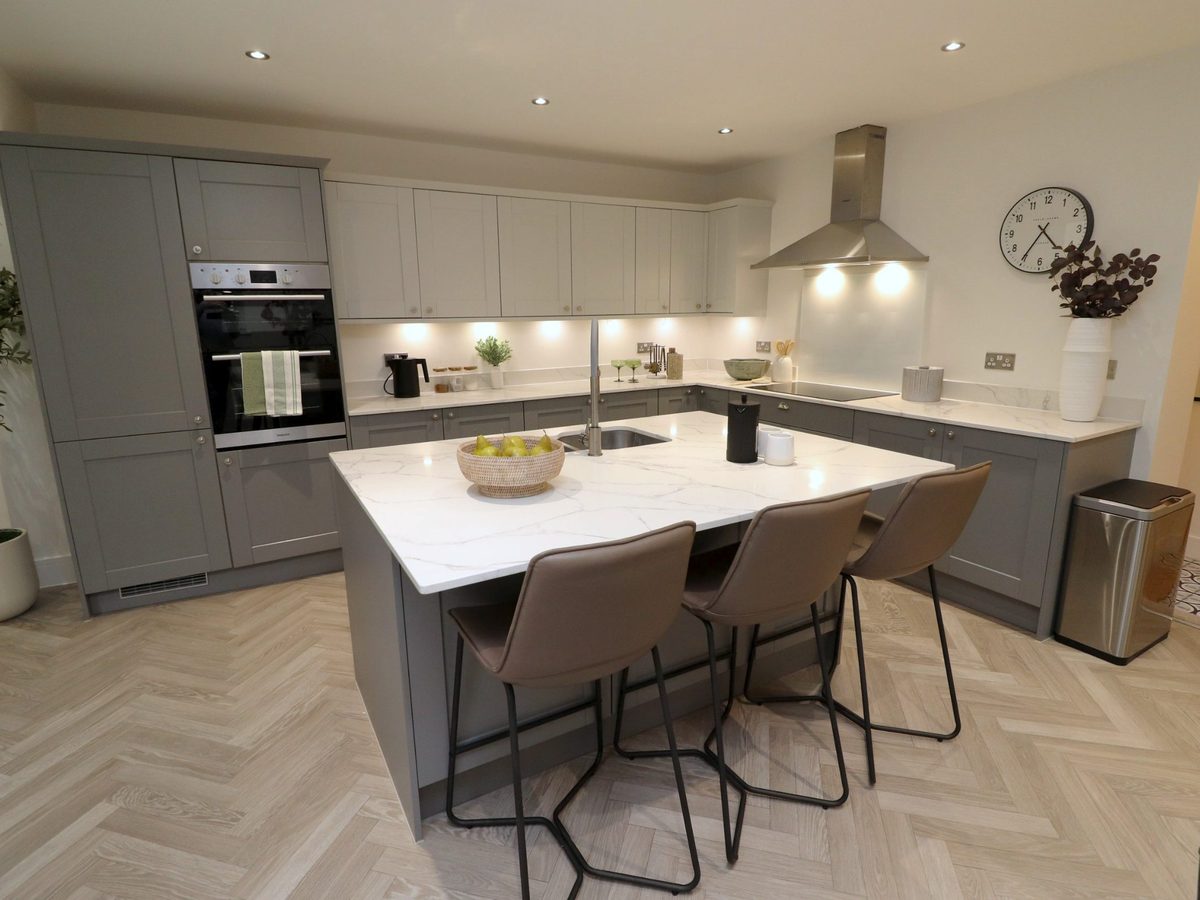 Staged kitchen: marble-topped island with leather bar stools, a bowl of pears and grey shaker units