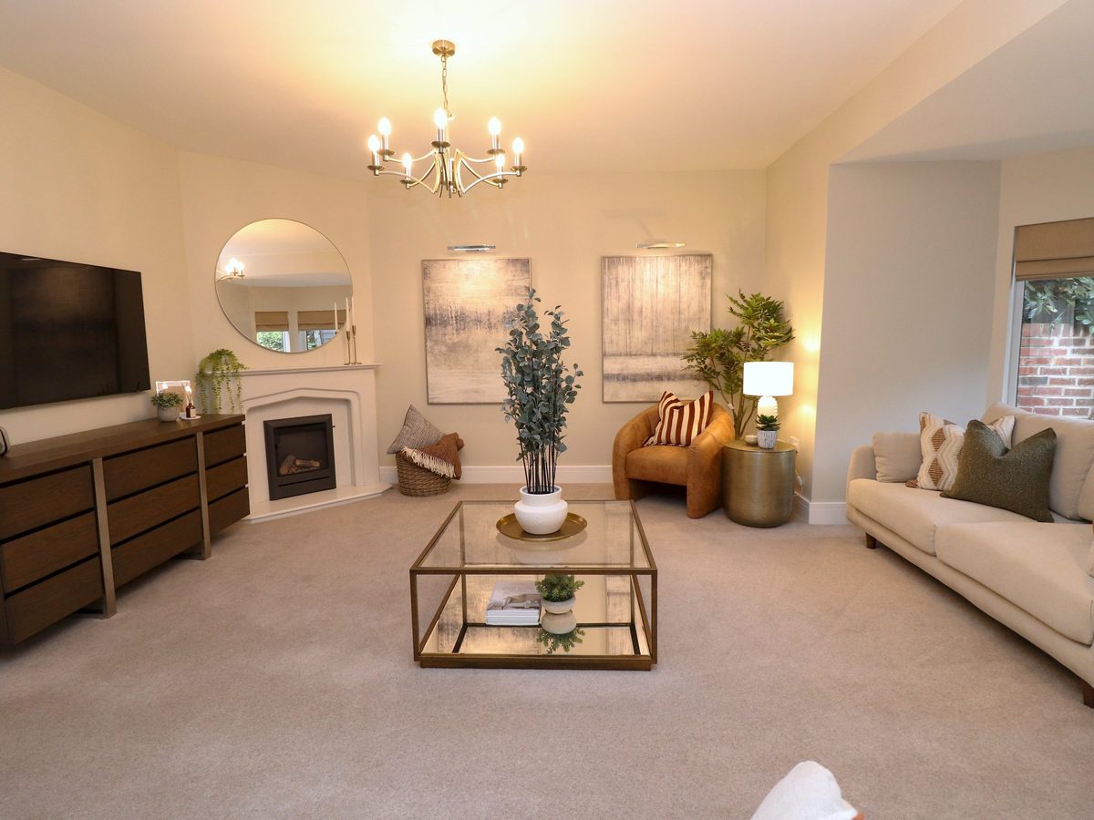 Staged lounge at Yew Tree Cottage: cream sofas, a tan leather armchair, lamps lit and the bay window beyond