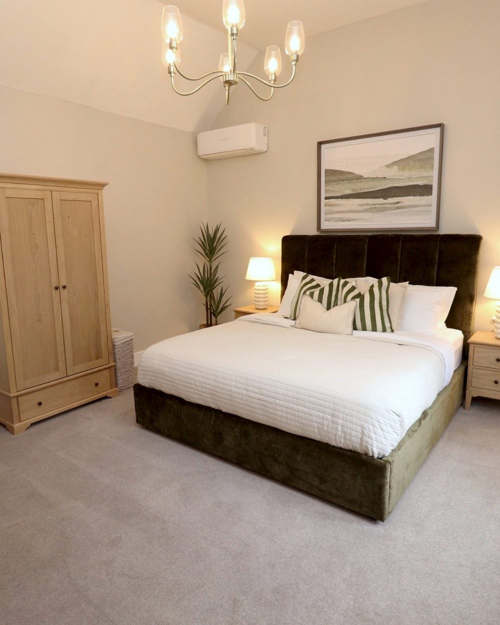 Staged main bedroom: olive velvet bed, oak wardrobe, lamps and a chandelier