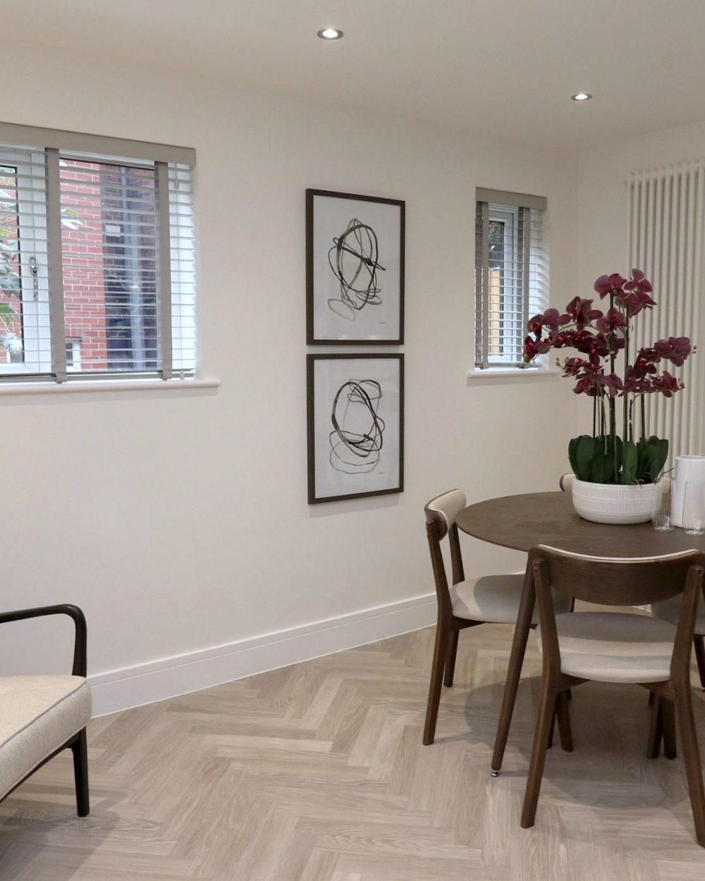 Family room with venetian blinds at two windows, framed line drawings, orchids on a round walnut table