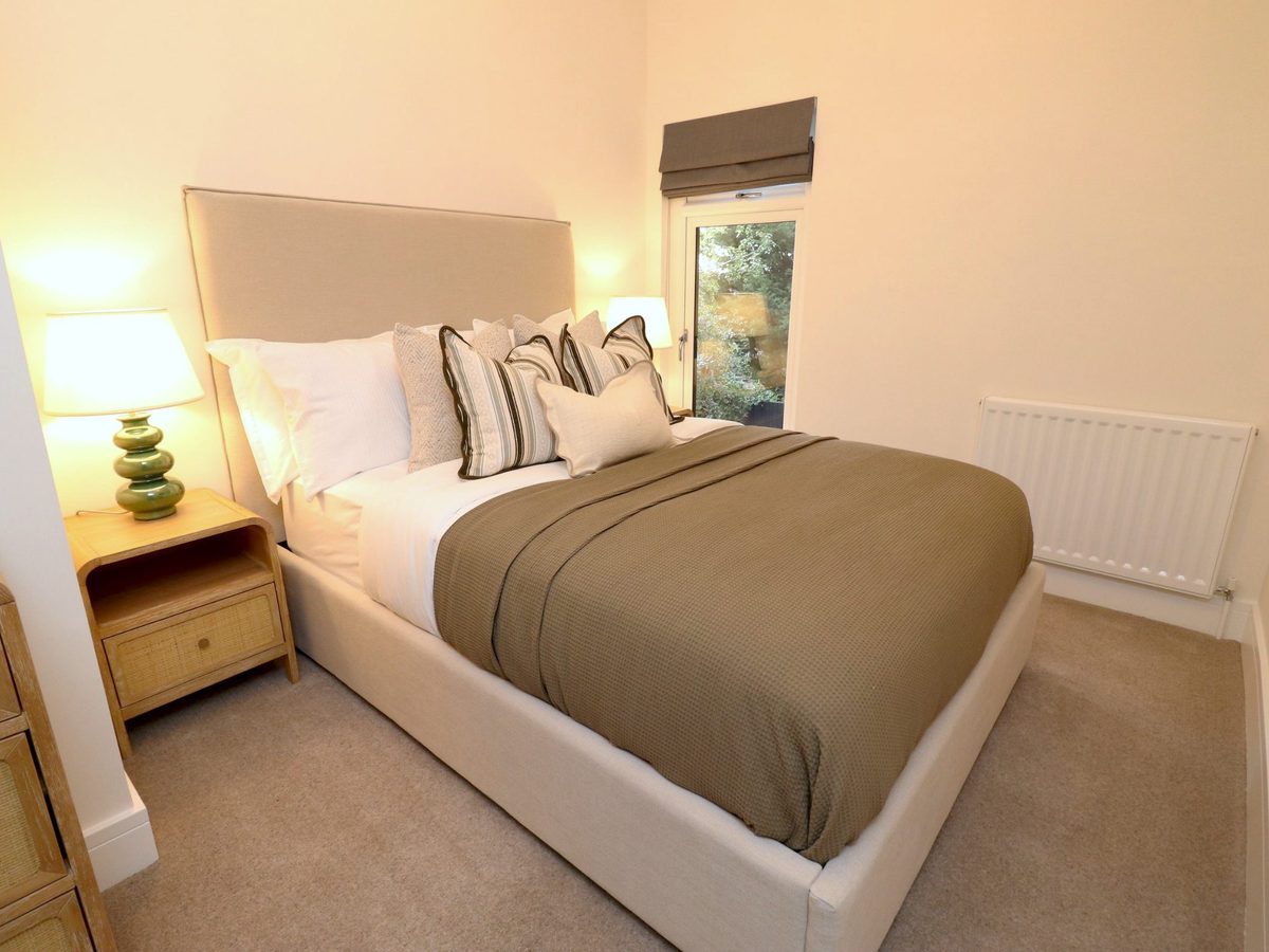 Staged second bedroom: dressed double bed with striped cushions, bedside lamp and a window with a blind