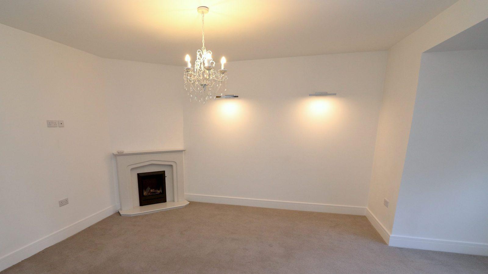 The living room at Yew Tree Cottage empty: bare walls, carpet, a chandelier and the fireplace