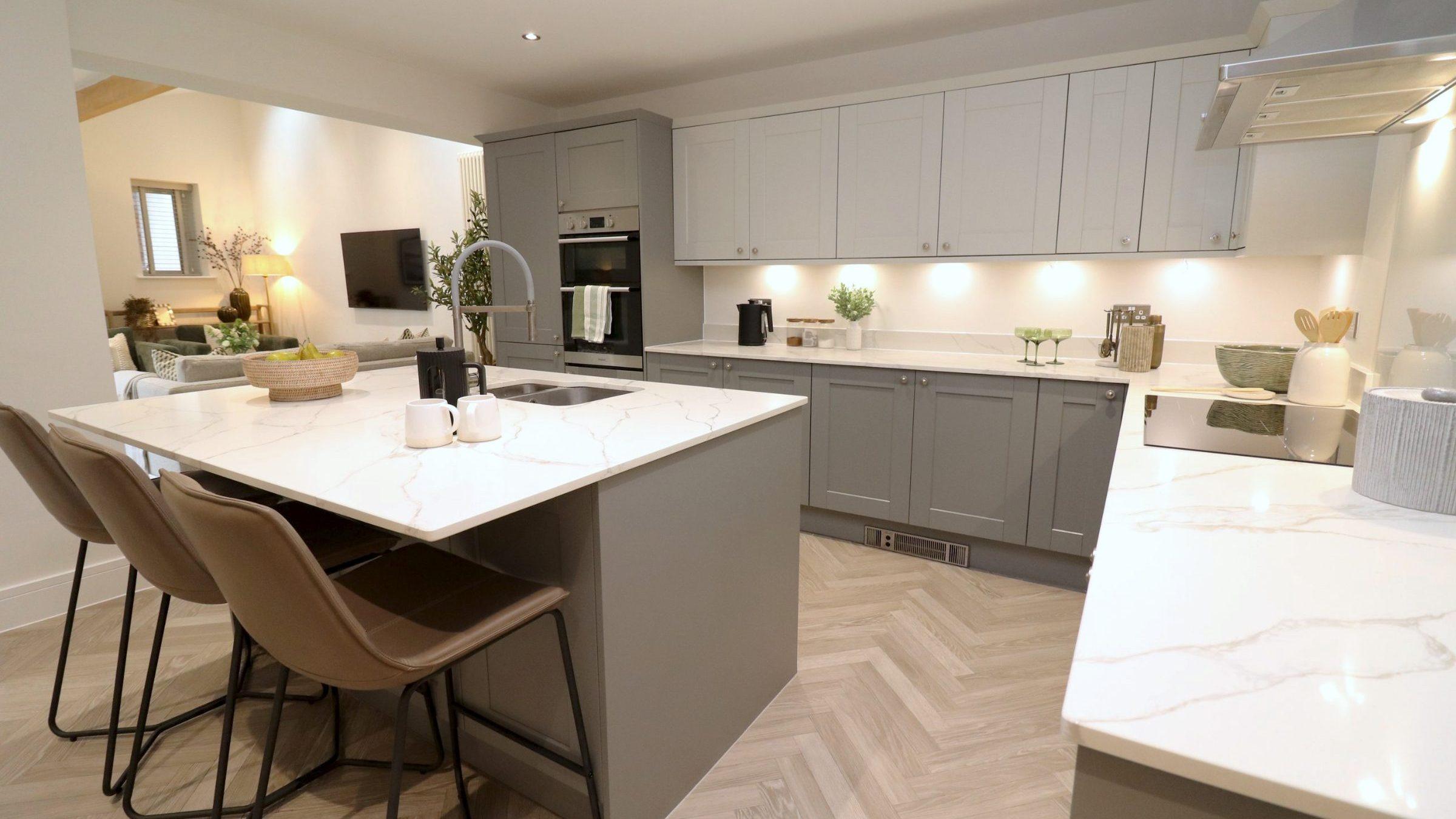 Yew Tree Cottage kitchen after staging: leather bar stools at the island, mugs and a bowl of pears, the family room beyond