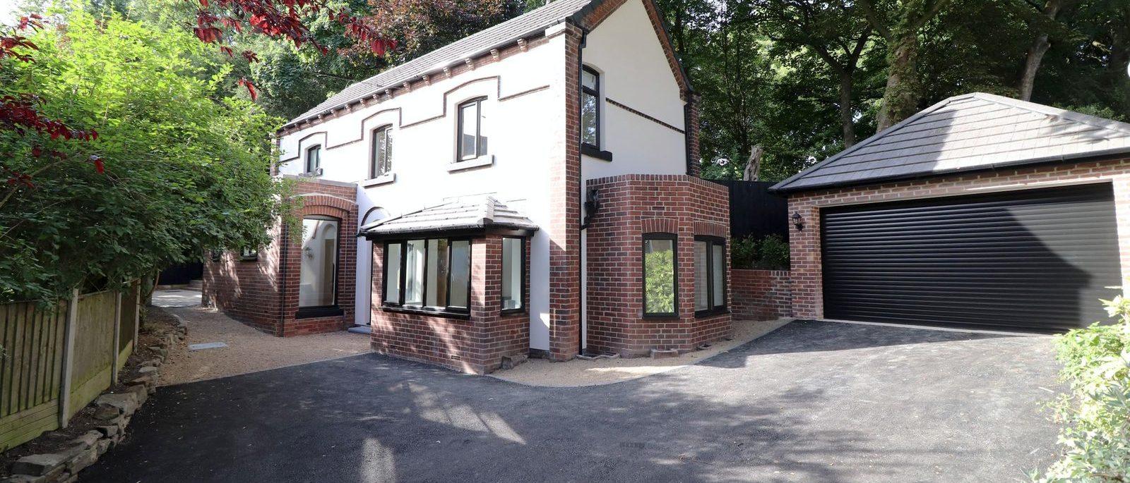 Yew Tree Cottage from the drive: white rendered house with red brick detailing, a bay window and a detached double garage among mature trees