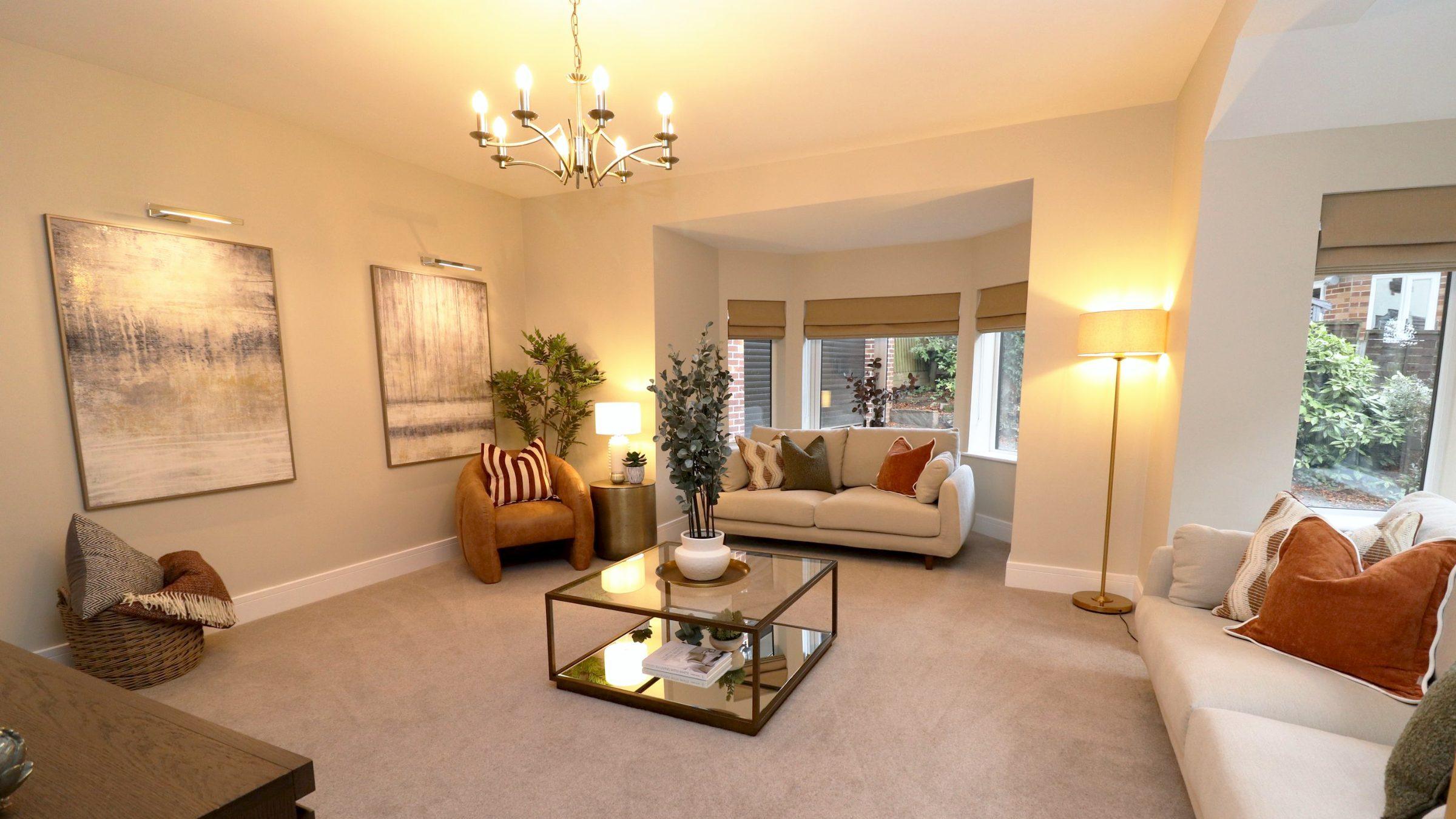 Yew Tree Cottage living room, staged by Curate Interiors: two cream sofas and a tan leather armchair around a glass coffee table, lamps lit, bay window beyond