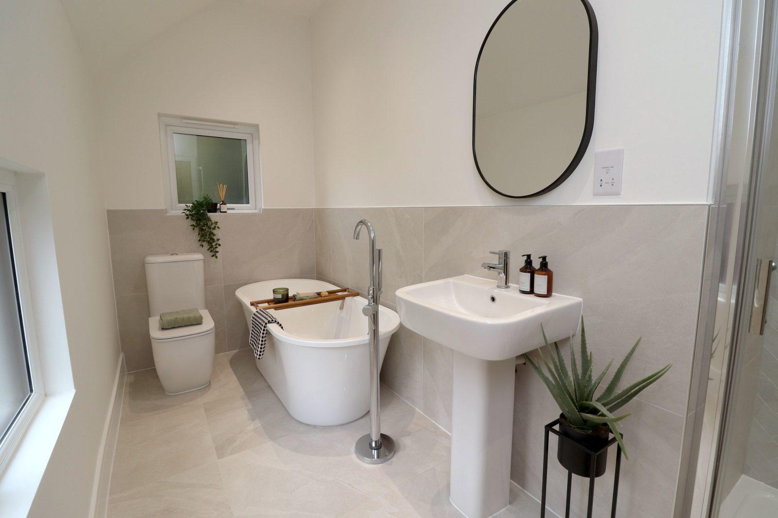 Bathroom: freestanding bath with a wooden caddy, basin, oval mirror and plants