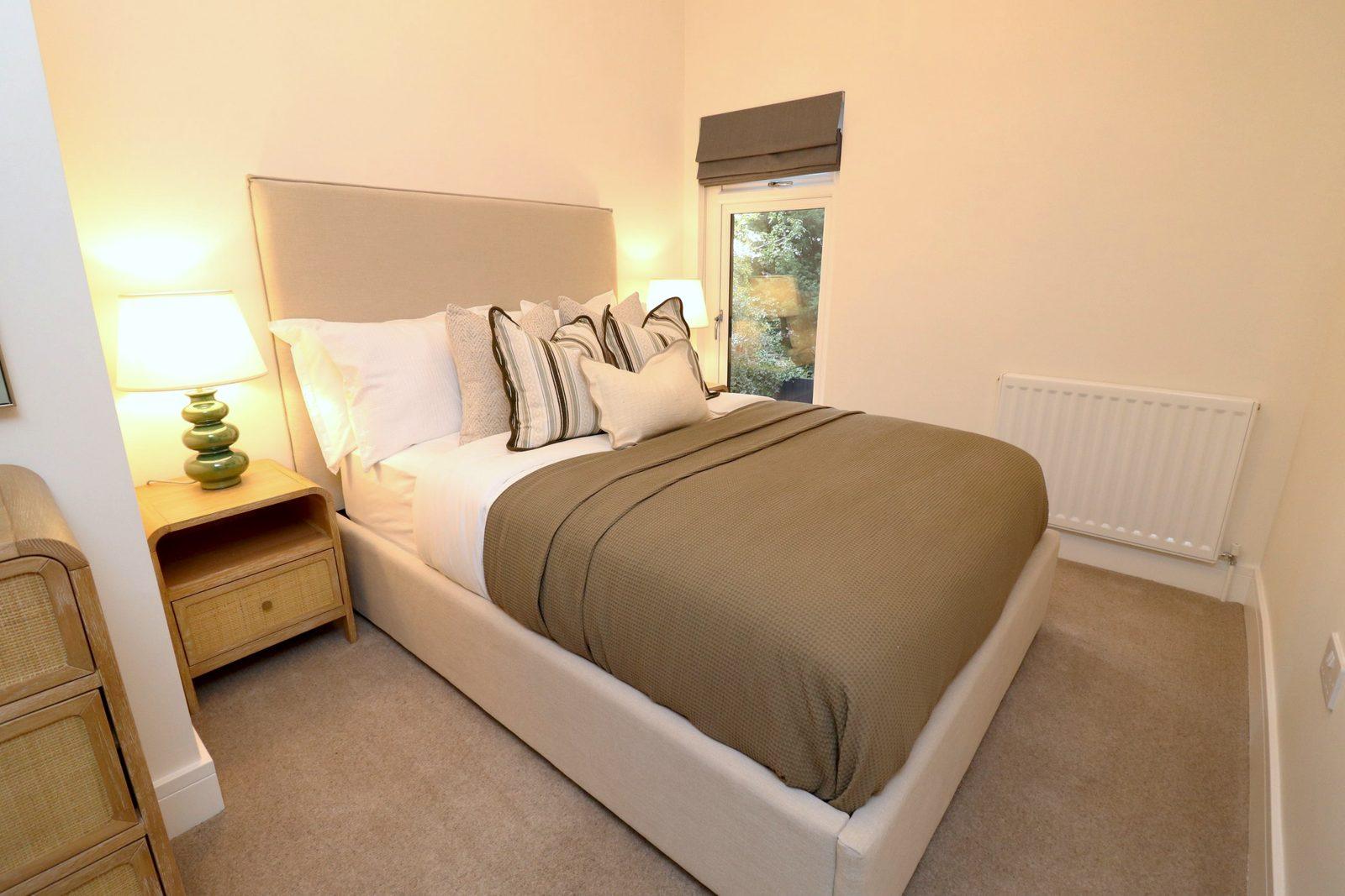 Second bedroom: dressed double with striped cushions, bedside lamp and the window beyond
