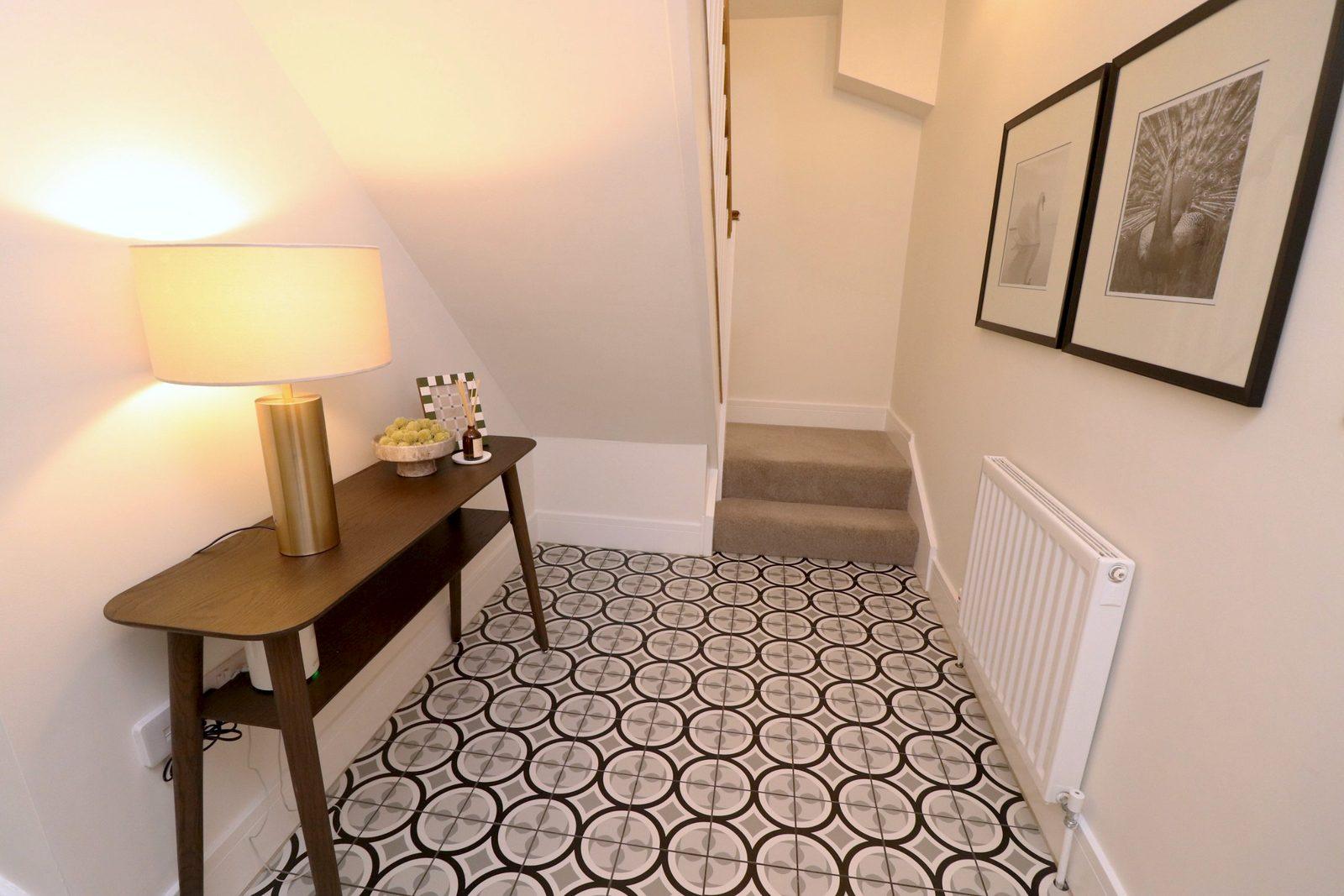 Entrance hall: walnut console with a brass lamp under the stairs, framed prints, patterned tiles