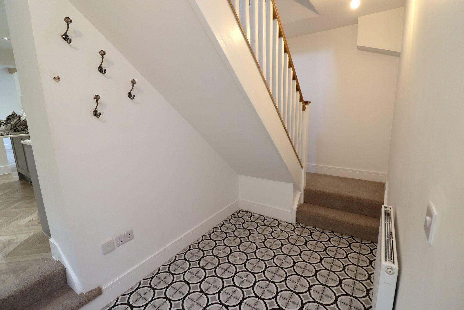 Hallway before: coat hooks on the wall, stairs, patterned floor tiles