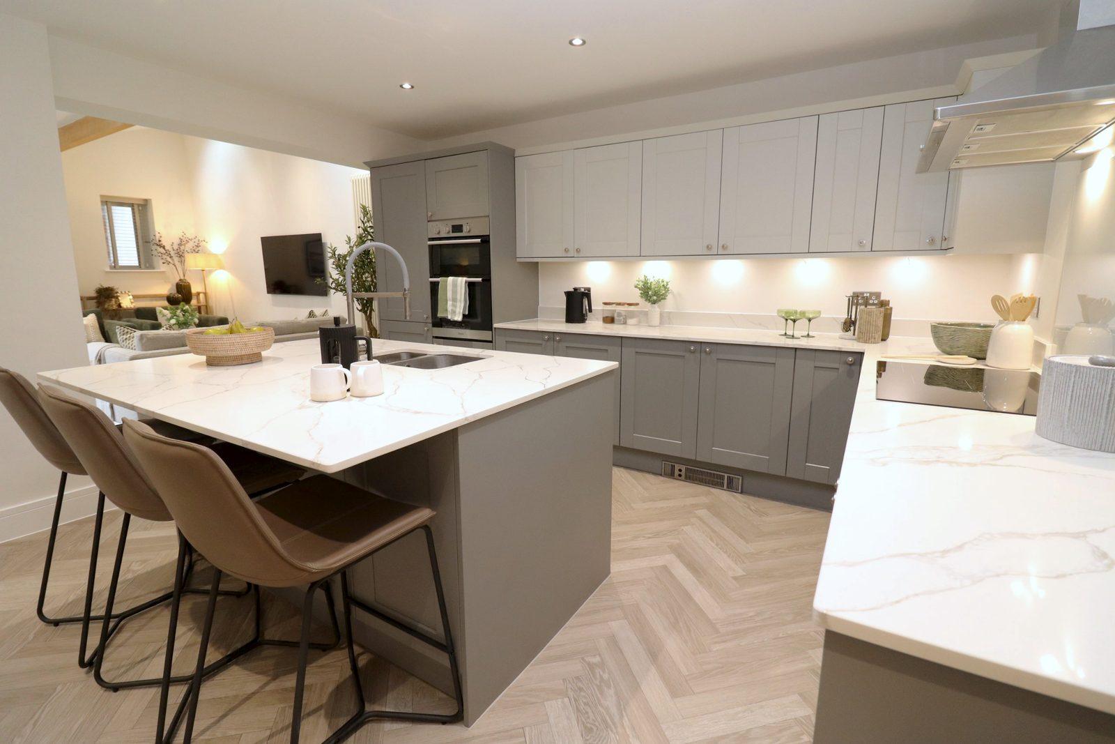 Kitchen after: leather bar stools at the island, a bowl of pears, mugs and the family room beyond