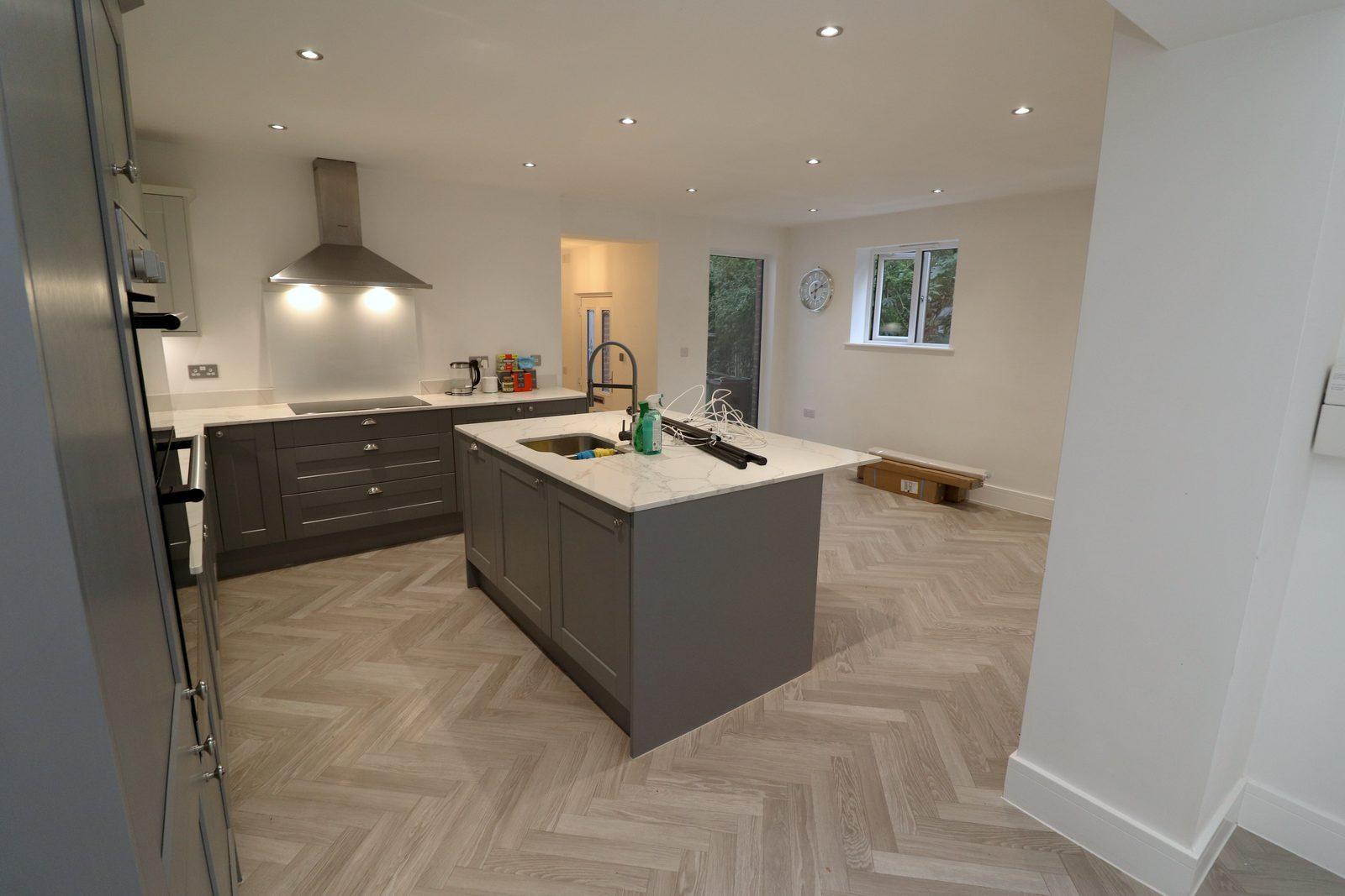 Kitchen before: grey shaker units, empty island, herringbone floor
