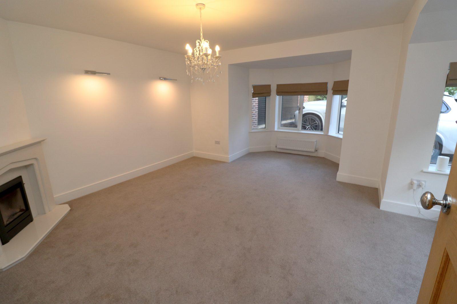 Living room before staging: empty carpeted room with a bay window and chandelier