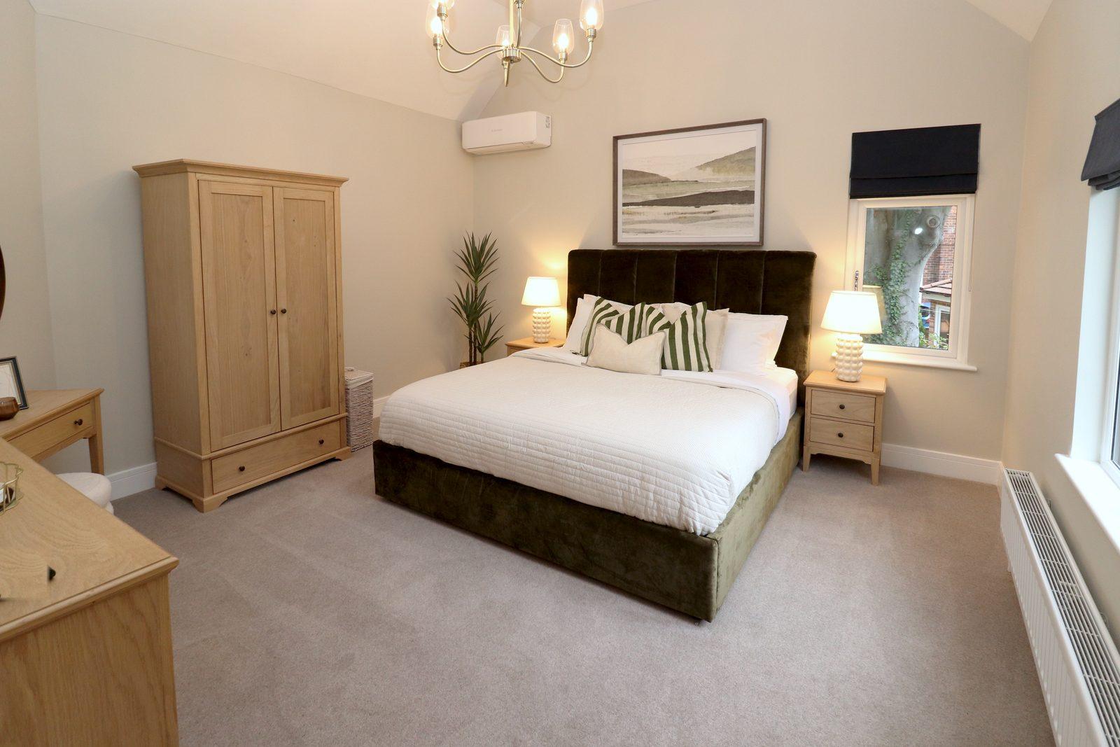 Main bedroom after: olive velvet bed with white linen, oak wardrobe, bedside lamps, landscape print